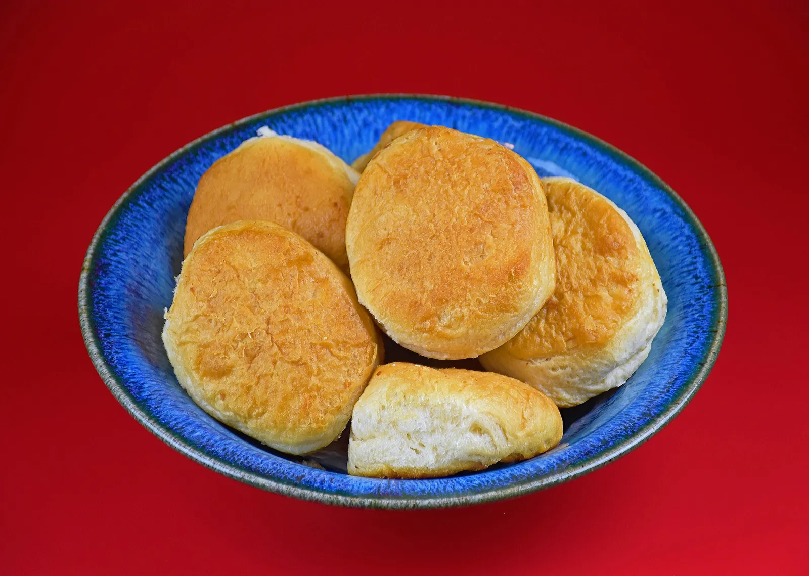 A blue bowl of golden biscuits on a red table